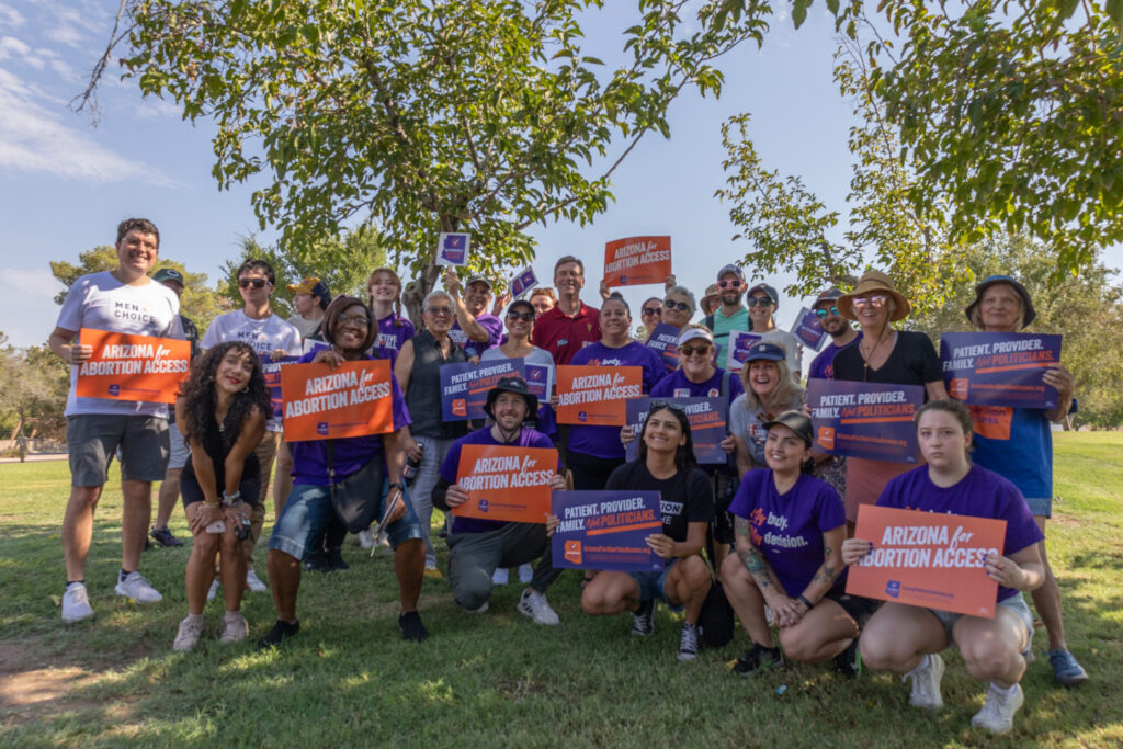 Large group of yes on prop 139 volunteers posing with Arizona Abortion Access signs at Kiwanis Park in Tempe, AZ under a shade tree